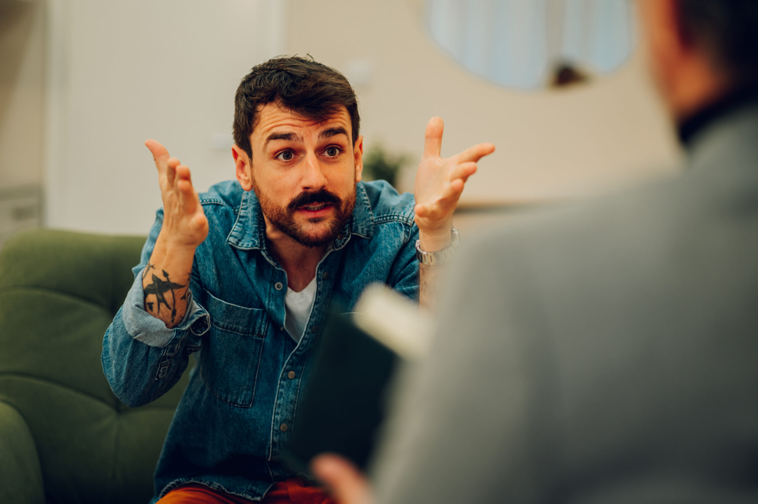 A furious client is expressing anger while sitting in an office on a sofa during his session with a shrink.