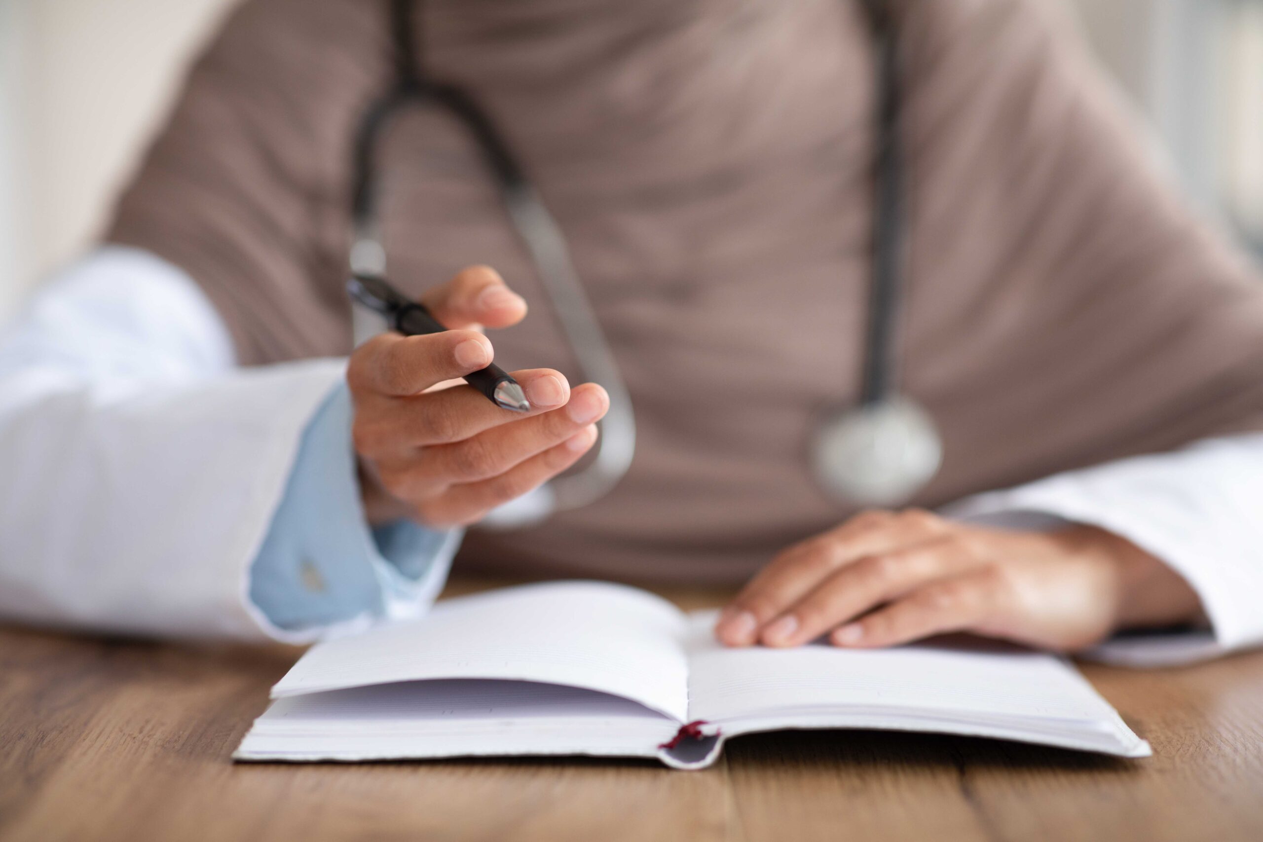 Closeup of female doctor holding pen, having notebook on workdesk